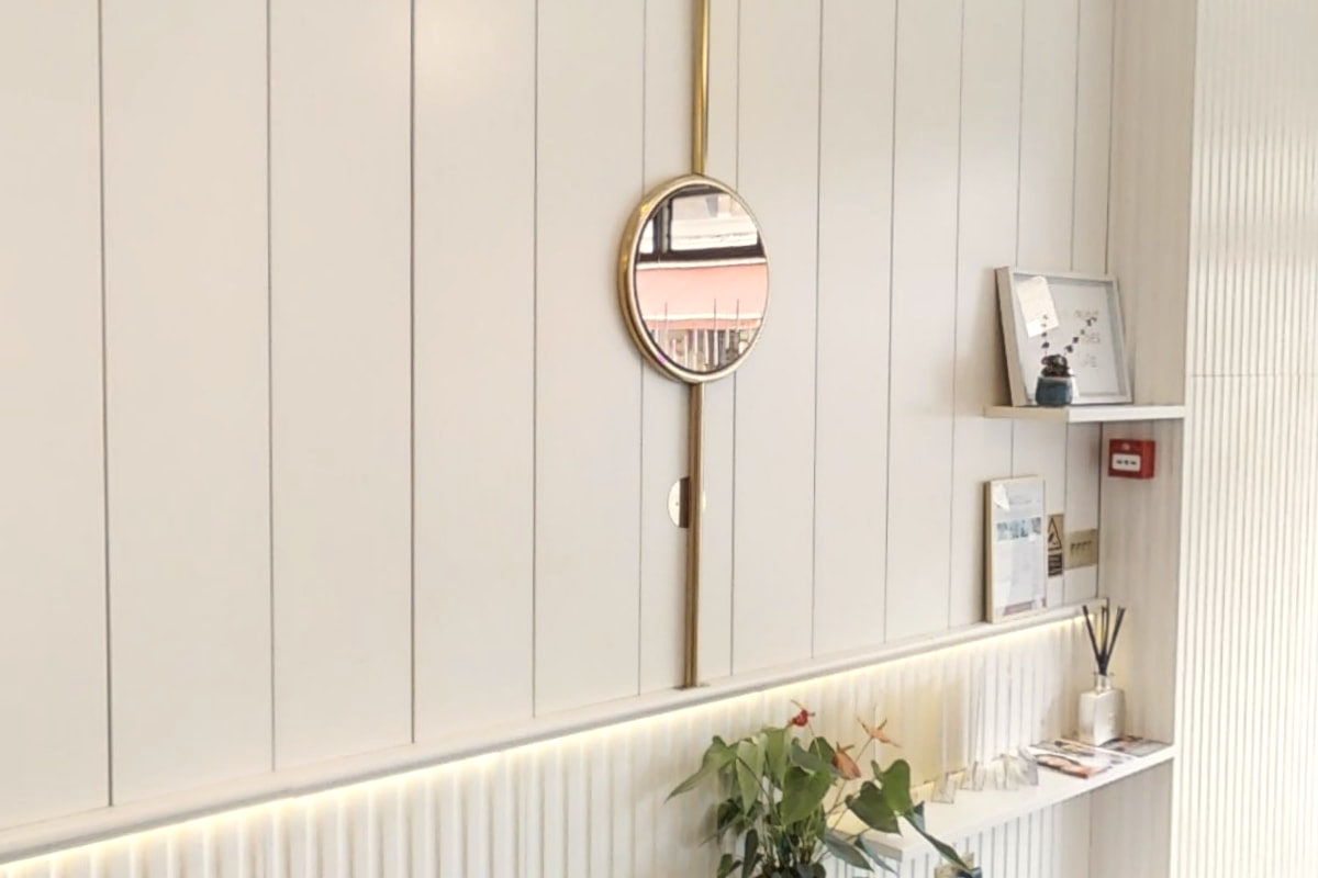 A round brass mirror on white panelling in the reception at Shirland Dental Practice