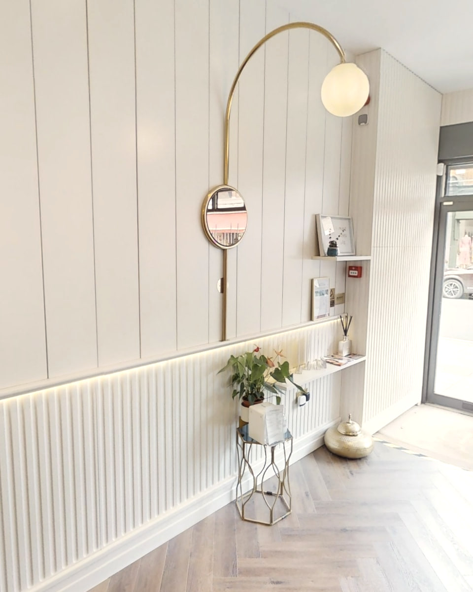 Reception at Shirland Dental Practice, with a brass arc lamp over a round mirror, a shelf and daylight from the street door